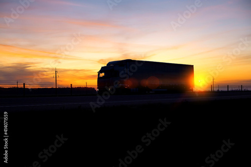 A truck with a semitrailer moves along the highway against the background of an evening sunset. Logistics and cargo transportation concept, driver fatigue while driving. Copy space for text
