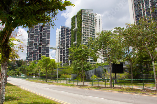 View at the street at Singapore with tall buildings in green grass and leaves, a lot of trees, empty road, ecological life, concept of modern life.