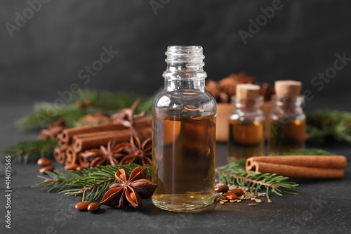 Bottle of essential oil, anise, cinnamon and fir tree branches on black table