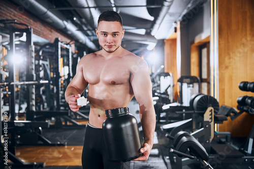 Smiling young bodybuilder taking supplements in gym