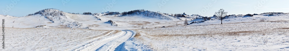 Panoramic view on snowy dirt road on the Tazheran steppe with snow-covered hills. Baikal region, Olkhon district. Winter landscape. Natural wide background, banner. Outdoors and winter travel