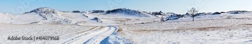 Panoramic view on snowy dirt road on the Tazheran steppe with snow-covered hills. Baikal region, Olkhon district. Winter landscape. Natural wide background, banner. Outdoors and winter travel
