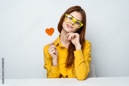 woman with a heart-shaped lollipop sits at a table in a yellow shirt