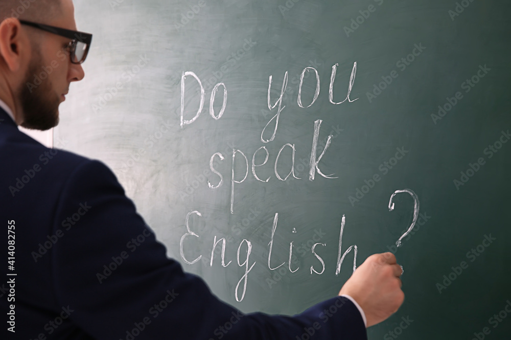 Teacher writing words Do You Speak English? on green chalkboard, closeup