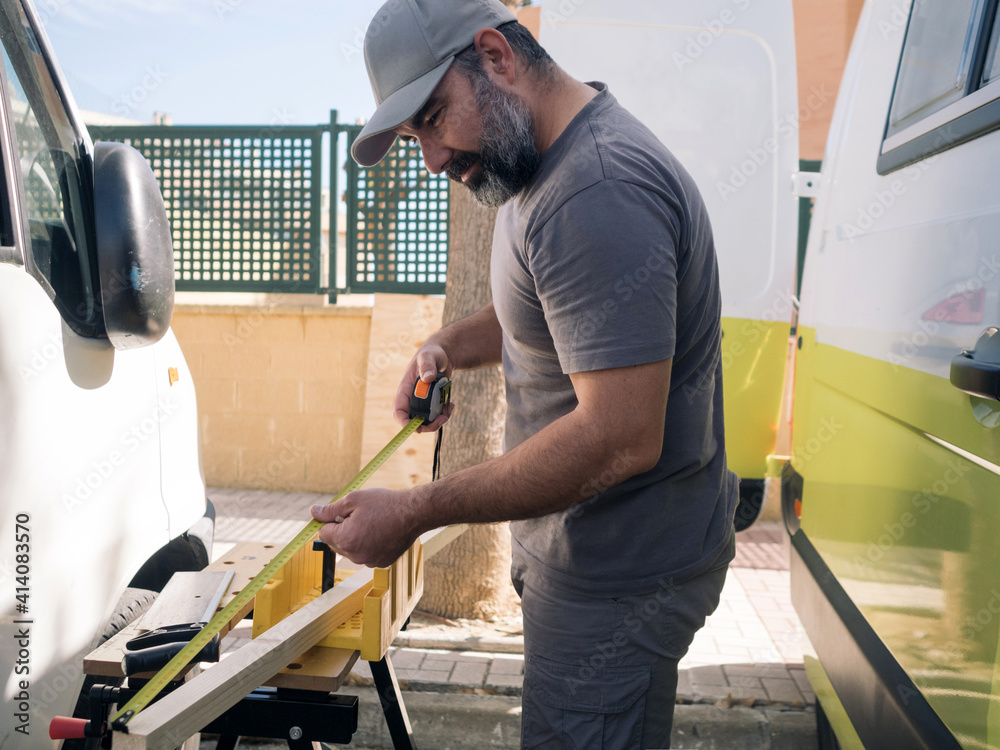Man measuring wood before cutting it. Self-construction of a camper van on the street. Man measuring wood before cutting it. Self-construction of a camper van on the street.