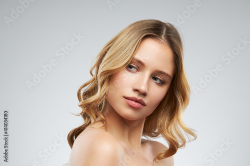 Cute blonde without makeup with clear and curly hair standing in studio and posing.