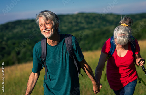 Active senior couple with backpacks hiking in nature.