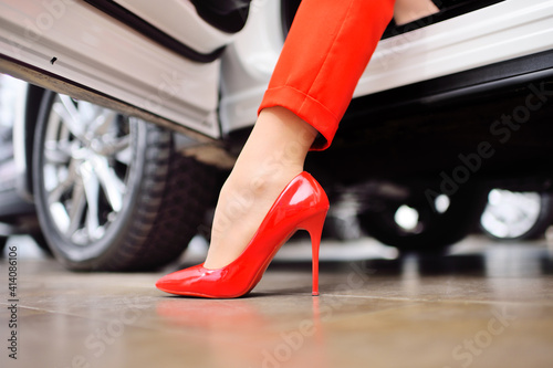 Obraz na płótnie close-up of a woman's leg in a red suit and red shoes against the background of a car