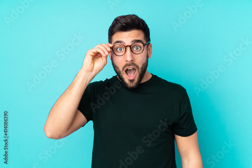 Caucasian handsome man isolated on blue background with glasses and surprised