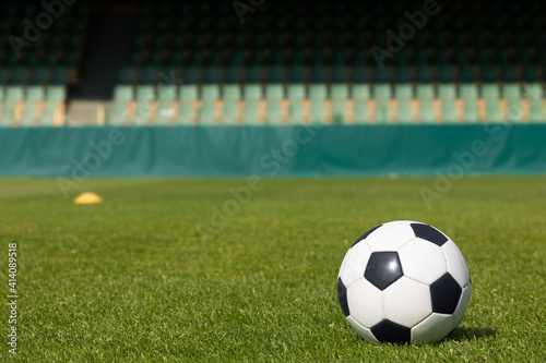 Classic Soccer Ball on Green Fresh Sports Turf. Football Stadium with Rows of Seats  in the Background © matimix