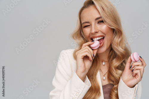 Beautiful happy girl in jacket winking while eating macaroons