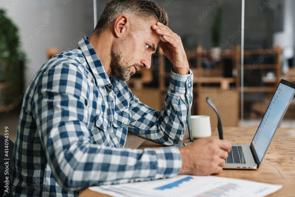 Brooding grey man working with laptop while sitting in office Brooding grey man working with laptop while sitting in office