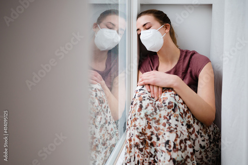 Young woman sitting indoor during the pandemic covid-19 corona time with ffp-2 mask in quarantine alone at home