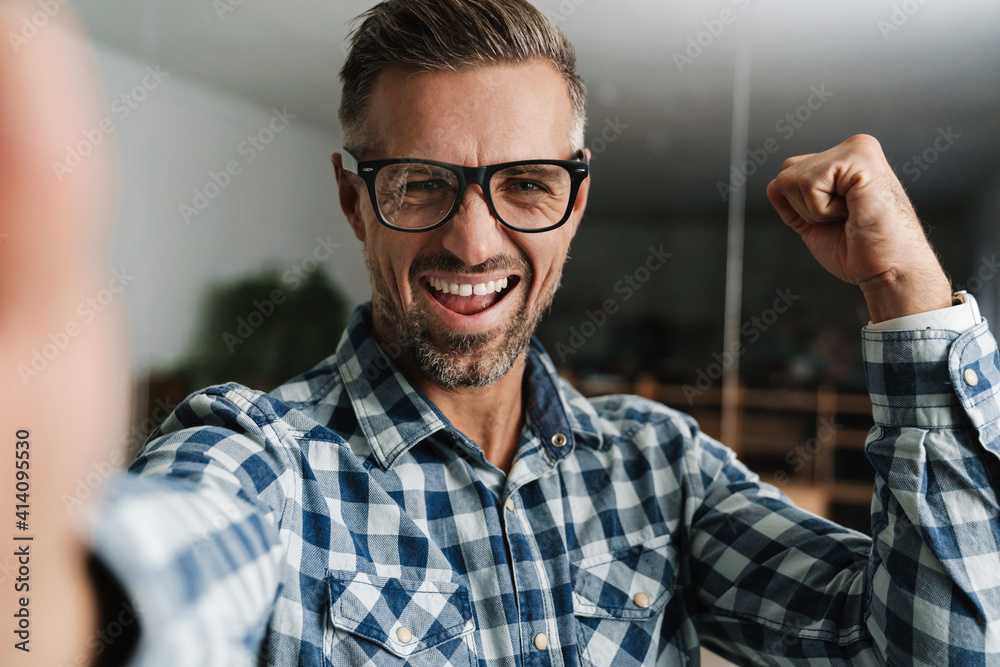 Excited white-haired man making winner gesture while taking selfie photo Excited white-haired man making winner gesture while taking selfie photo