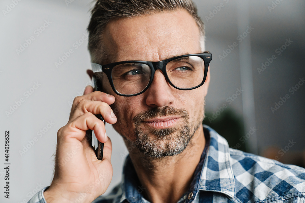 Focused white-haired man in eyeglasses talking on cellphone in office Focused white-haired man in eyeglasses talking on cellphone in office