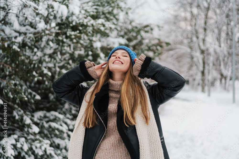 Happy beautiful girl in knit hat smiling while walking in winter park