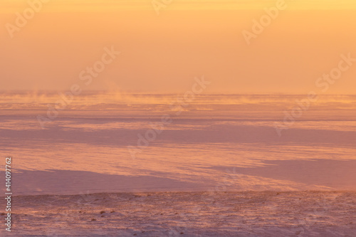 Winter arctic landscape. Morning aerial view of snowy tundra and frozen sea. Cold windy and frosty weather. Blowing snow. Beautiful golden light at sunrise. Chukotka  Polar Siberia  Far North Russia.