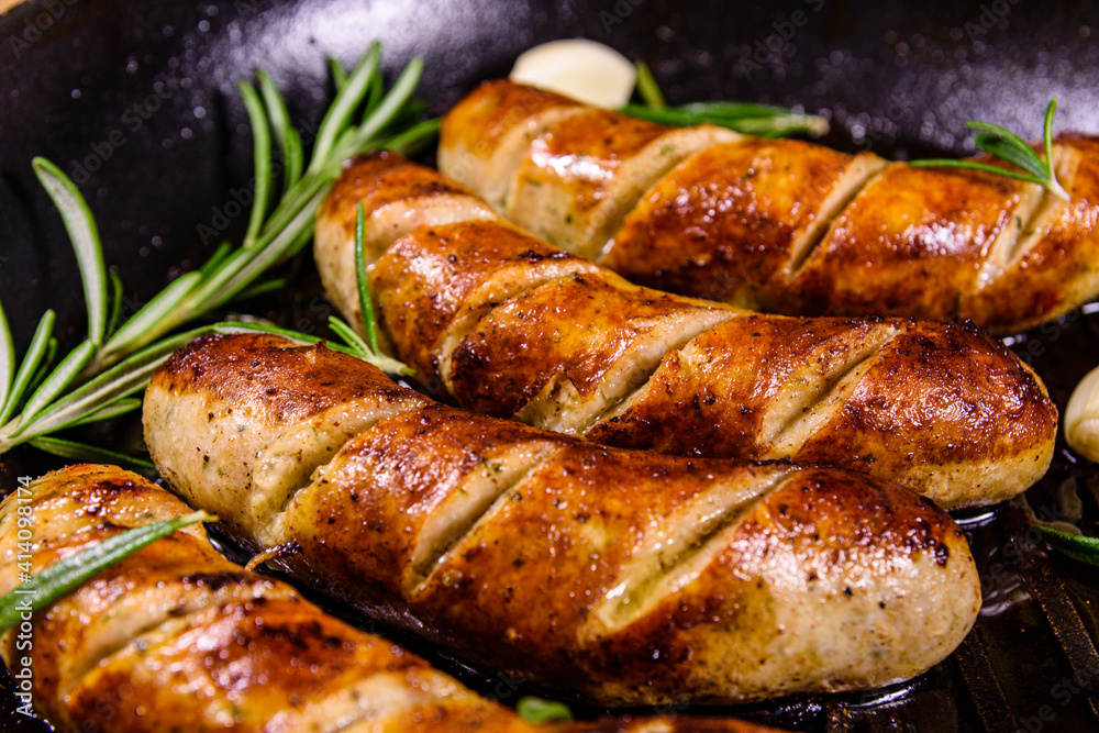 Roasted sausages with rosemary twigs and garlic in a cast iron grill pan