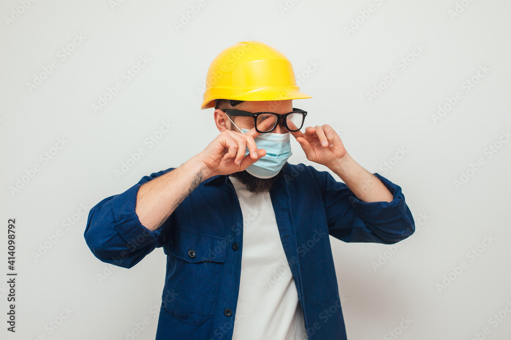 The worker wiping blurred foggy misted glasses caused by wearing medical mask on light background. Covid-19. Difficulties in work The worker wiping blurred foggy misted glasses caused by wearing medical mask on light background. Covid-19. Difficulties in work