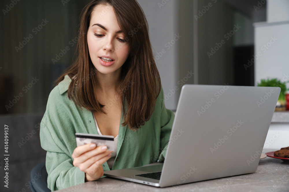 Focused nice woman using credit card while working with laptop Focused nice woman using credit card while working with laptop