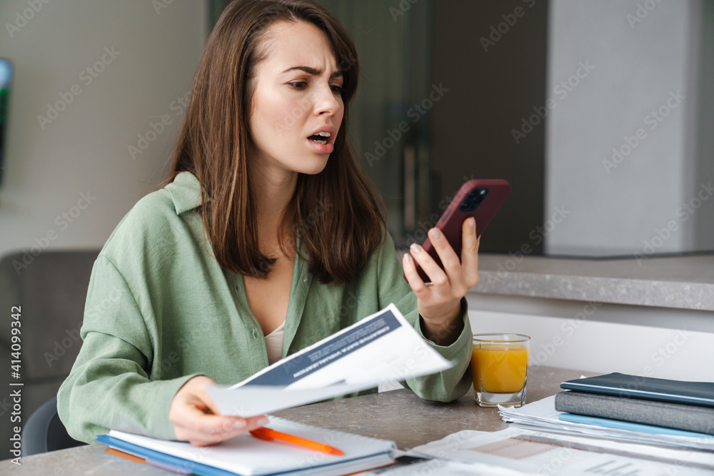 Outraged young woman using mobile phone while working with papers Outraged young woman using mobile phone while working with papers