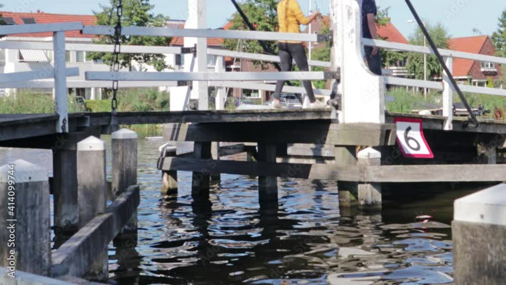Wooden foot bridge crossing a canal. Legs of people walking over the bridge visible Wooden foot bridge crossing a canal. Legs of people walking over the bridge visible
