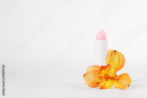White tube of pink lip balm or gloss, to protect and nourish the lips, near the astelmeria flower, isolated on a white background. Spring season cosmetics. Gift idea for a woman. Copy space photo