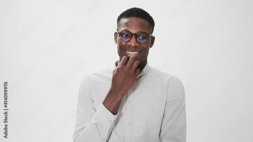 A surprised african american man wearing glasses is thinking about something standing isolated over white background in studio A surprised african american man wearing glasses is thinking about something standing isolated over white background in studio