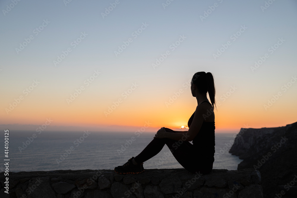 Backlit silhouette of a woman watching the sunrise over the sea