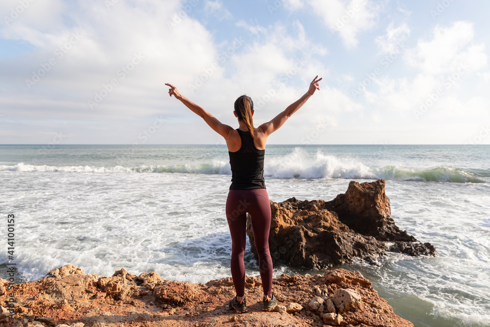 Attractive woman watching the waves while doing the victory sign. Healthy lifestyle concept