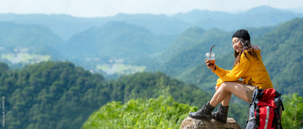 Asian women hiker or traveler with backpack adventure sitting and drinking ice coffee relax and rest on the mountain outdoor for destination leisure education nature on vacation