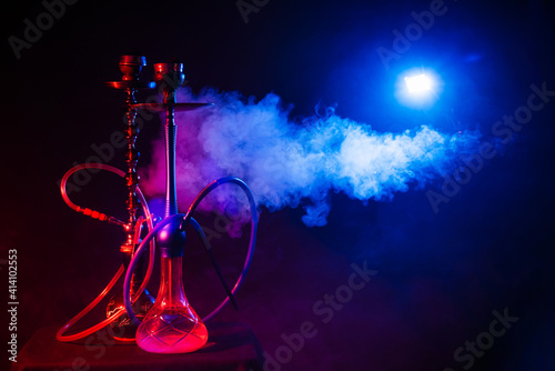 Hookah, shisha on a smoky black background with neon lighting and smoke. Place for your text © Anastasia