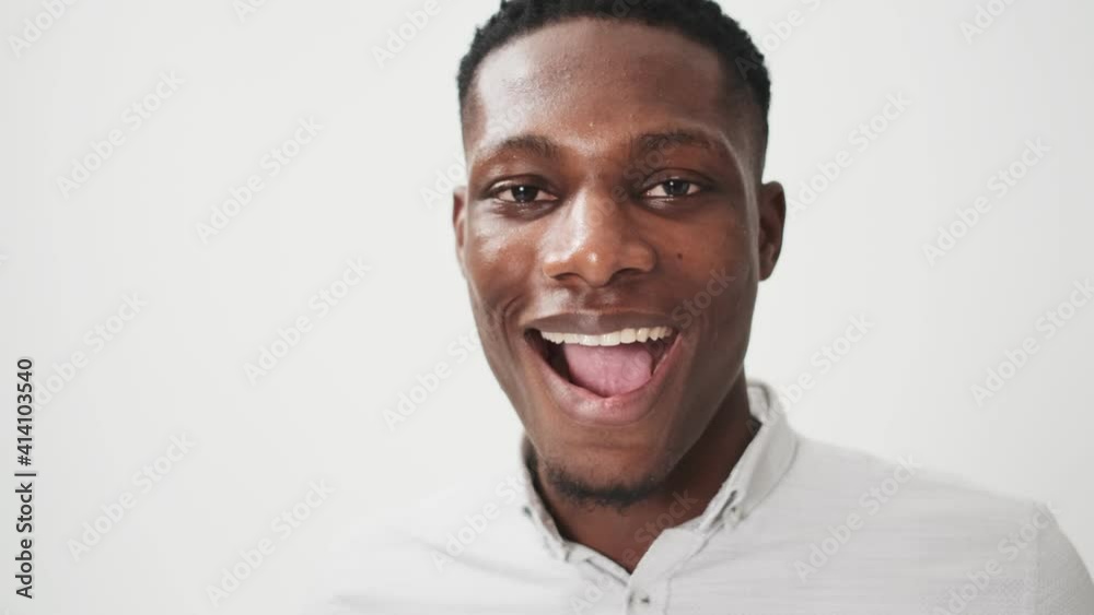 A close-up view of a surprised african american man is looking to the camera standing isolated over white background in studio A close-up view of a surprised african american man is looking to the camera standing isolated over white background in studio
