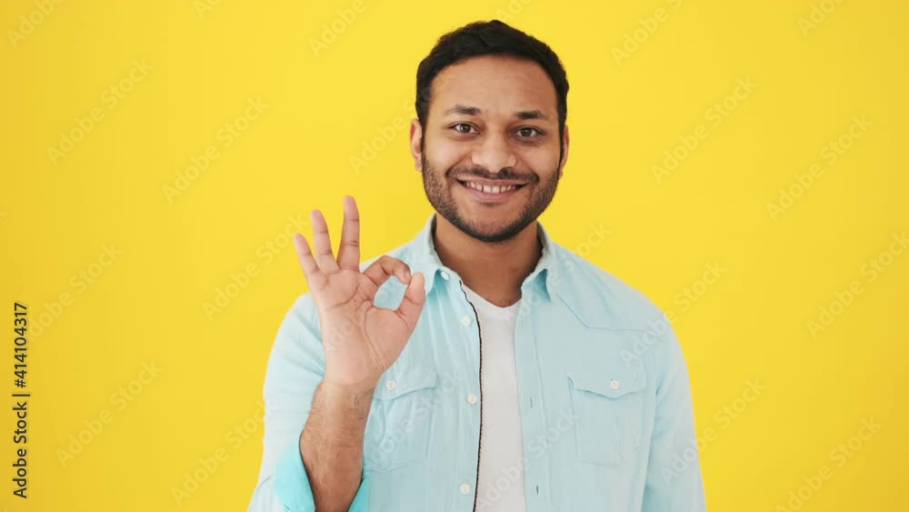 A handsome indian man is showing OK gesture standing isolated over yellow background in studio A handsome indian man is showing OK gesture standing isolated over yellow background in studio