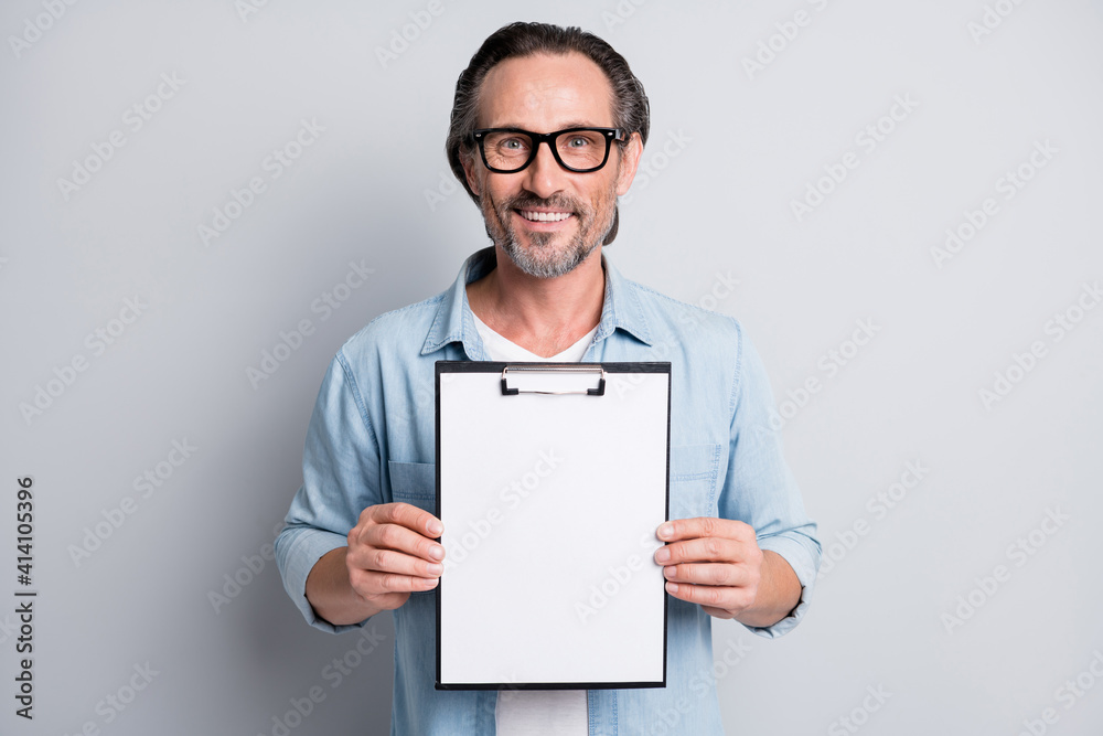 Photo of handsome man happy positive smile hold clipboard show document isolated over grey color background Photo of handsome man happy positive smile hold clipboard show document isolated over grey color background