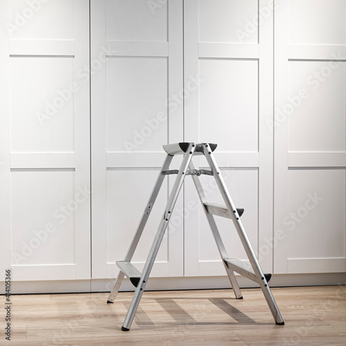 The folding ladder for repair and installation of furniture stands on a wood floor. Repair