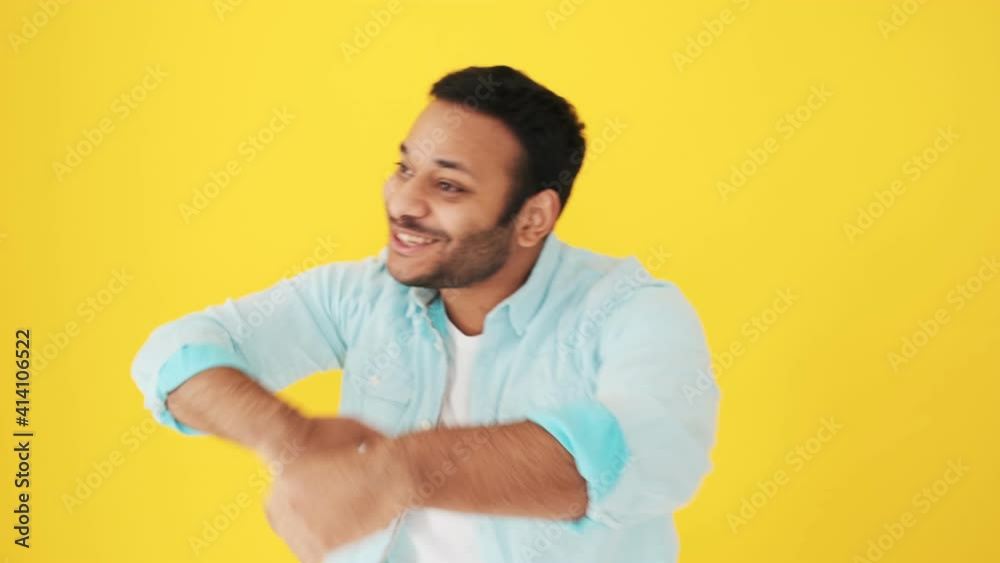 A happy indian man is inviting people to the dance floor while dancing isolated over yellow background in studio A happy indian man is inviting people to the dance floor while dancing isolated over yellow background in studio