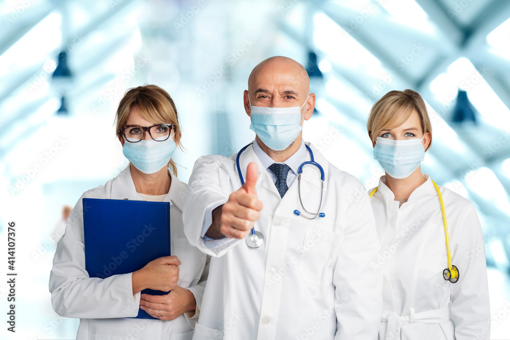 Group of medical team wearing face masks while male doctor giving thumbs up Group of medical team wearing face masks while male doctor giving thumbs up
