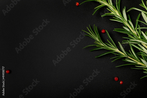 Sprigs of fresh rosemary and pink pepper grains of Schinus terebinthifolius on dark background. Workpiece or blank for a culinary-themed design. Top view