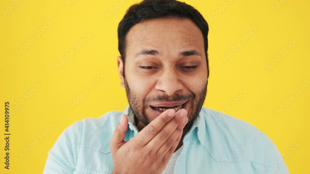 A close-up view of a sleepy indian man is yawning standing isolated over yellow background in the studio A close-up view of a sleepy indian man is yawning standing isolated over yellow background in the studio