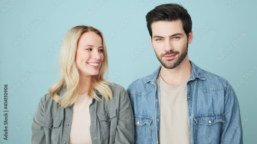 Happy couple man and woman are smiling to the camera while standing isolated over blue background in studio Happy couple man and woman are smiling to the camera while standing isolated over blue background in studio