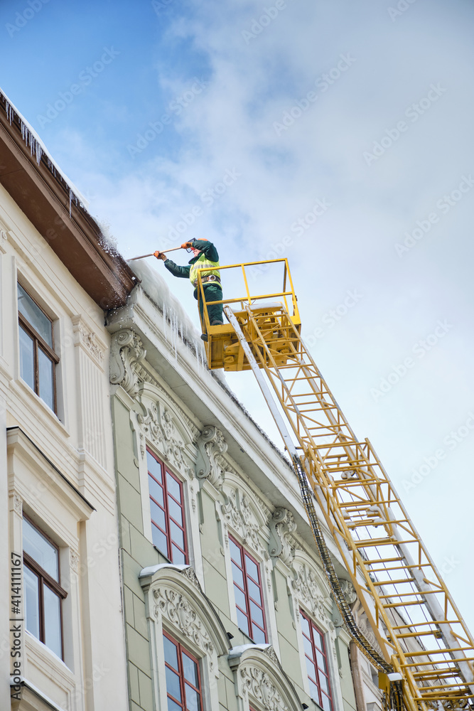 Fototapeta premium Public utilities on special vehicles remove icicles from the roofs of houses on the Rynok square in Lviv. Roof Winter Workers.