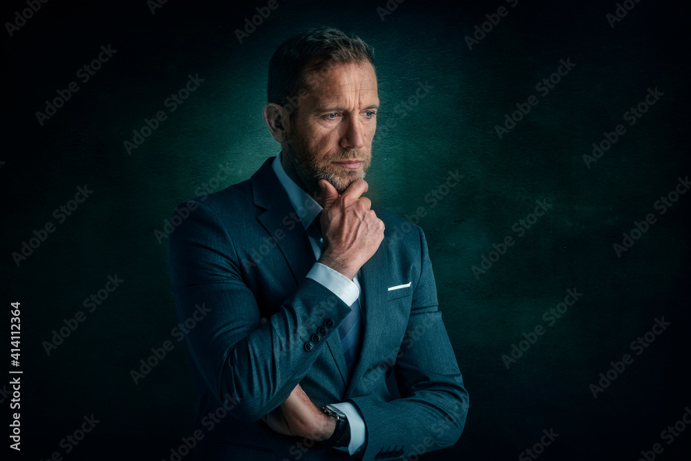Studio portrait of businessman looking deep in thought while standing at isolated dark background Studio portrait of businessman looking deep in thought while standing at isolated dark background