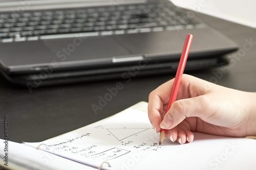 Young girl - female student writes homework from math at home. He writes in pencil in a notebook and counts.