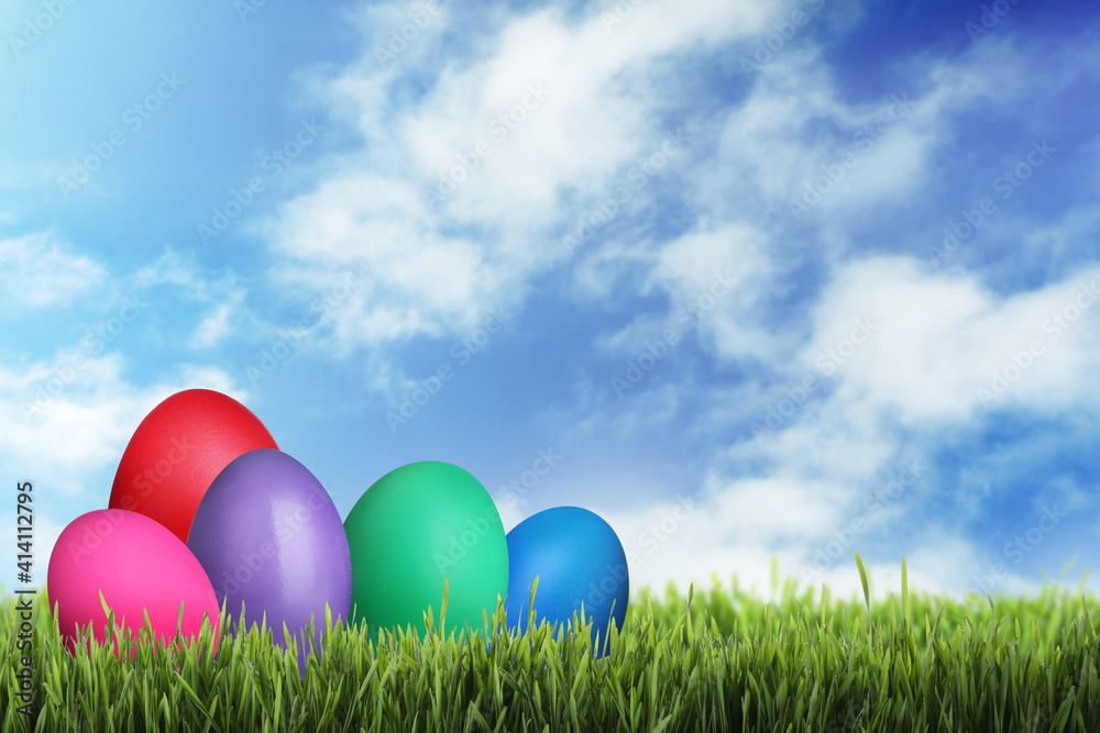 Bright dyed Easter eggs on green grass outdoors, space for text
