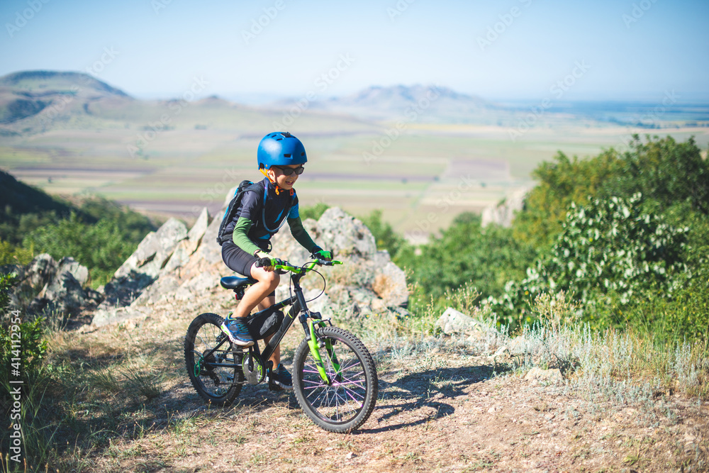 Fototapeta premium Happy kid boy of 8 years having fun in summer park with a bicycle on beautiful fall day. Active child wearing bike helmet
