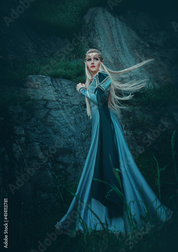 Beautiful fantasy woman elven goddess walks in nature mystical forest. Long creative vintage blue dress, sleeves. Blond hair fluttering in motion. Fairy cute face. Art Girl elf princess fashion model photo