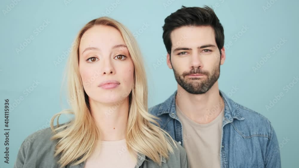 Confident couple man and woman are showing negative gesture standing isolated over blue background in studio Confident couple man and woman are showing negative gesture standing isolated over blue background in studio