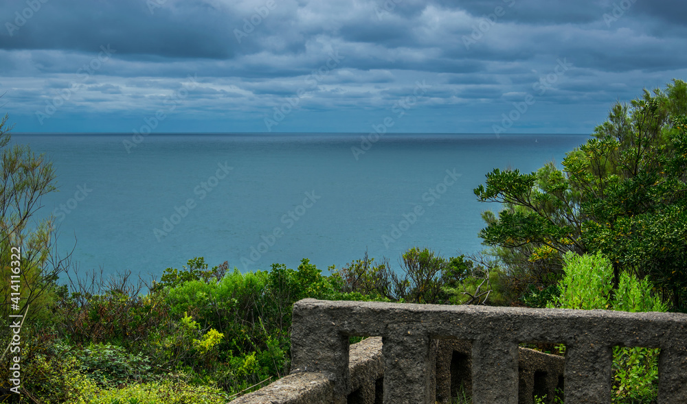 Nubes, mar, vegetación costera y la valla de piedra de un mirador