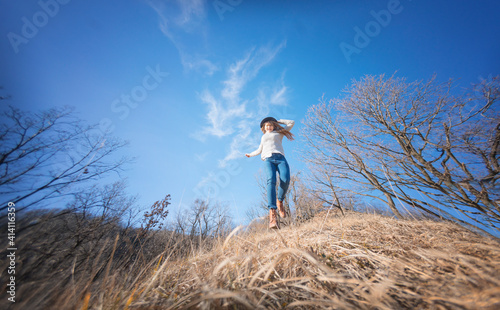 Young happy cheerful woman in hat jumping on blue sky background in spring forest